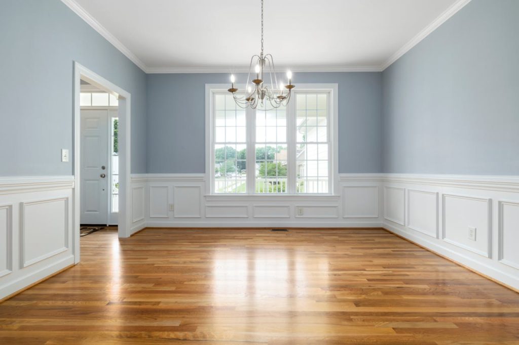 Bright empty room featuring a chandelier, wooden floor, and large windows.